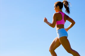 Woman in shorts and sports bra jogging against a blue sky