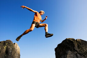 Man taking a big leap, jumping from a big rock to another
