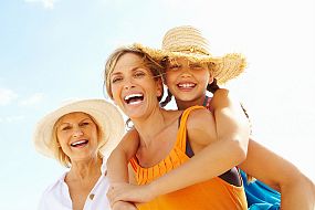 Three generations -  daughter, mother and grandmother, smiling at the beach, wearing sun hats