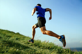 Man running up hill on green grass against a blue sky