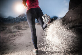 Woman jogging in sports gear kicking sand behind her