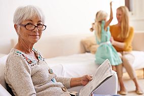 Grandmother reading the paper with daughter and granddaughter in the background