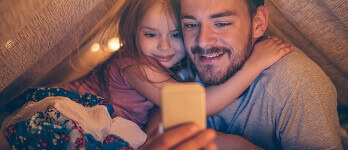 Father with his daughter in a tent looking at a phone screen Father with his daughter in a tent looking at a phone screen