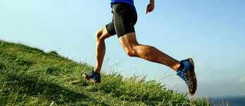 Man running up hill on green grass against a blue sky Man running up hill on green grass against a blue sky