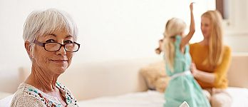 Grandmother reading the paper with daughter and granddaughter in the background