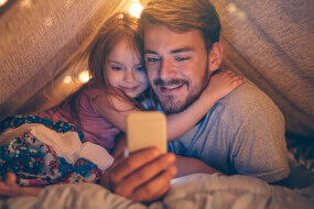 Father with his daughter in a tent looking at a phone screen